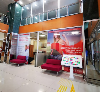 مدخل مستشفى Medical Park في تركيا مع لافتات إعلانية لخدمات علاج السمنة ومقاعد انتظار حمراء